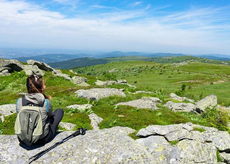 Randonneuse assise sur un sommet rocheux contemplant le vaste panorama de pâturages d'altitude des hautes chaumes des monts du Forez